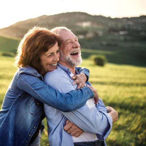 A Couple Hugs Out in a Field While Laughing
