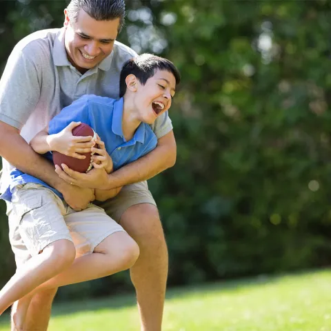 A father playfully tackles his son as they play football outside.