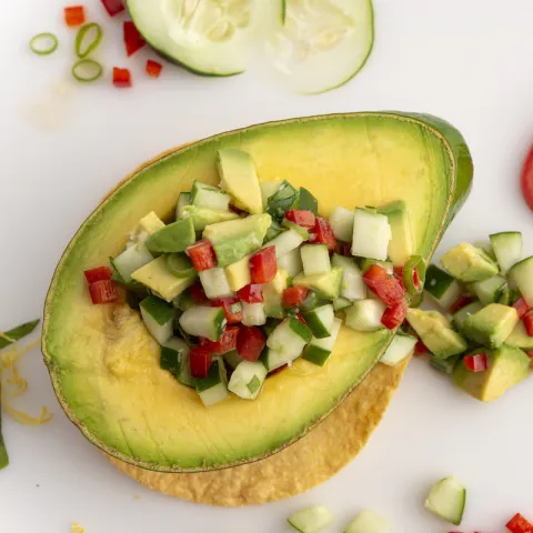 Half an avocado filled with avocado salsa on a white surface