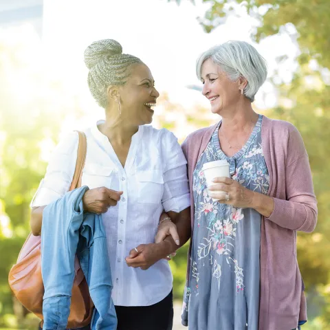 Two Women Walk Through a Park Together Drinking Coffee