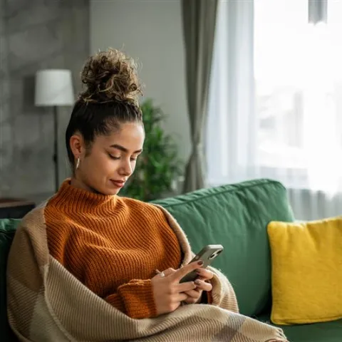 Woman sitting on green couch and looking at her phone.