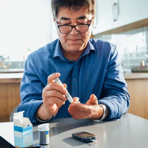 A man sitting in a kitchen using a glucose monitor.