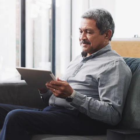 Senior Man looking at tablet sitting on couch.