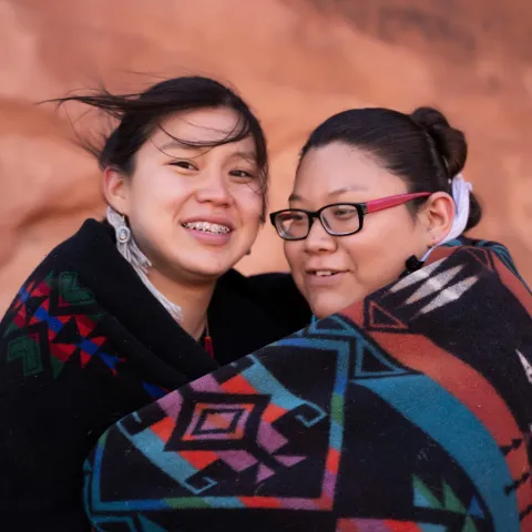 Native American mother and daughter wrapped in a blanket together while outdoors.