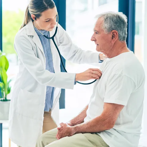 A female physician examining an older man's breathing with a stethoscope. 