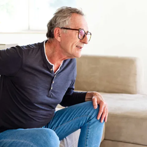 A senior gentleman showing discomfort while getting up from his couch