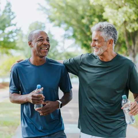 Two men walking outdoors together while holding water bottles.