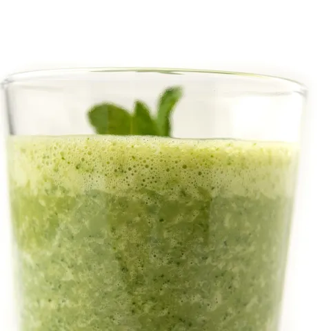 Clear glass of green smoothie with sprig on top.