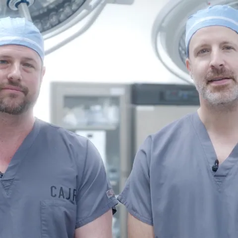 Two surgeons wearing scrubs and surgical caps standing together in an operating room.