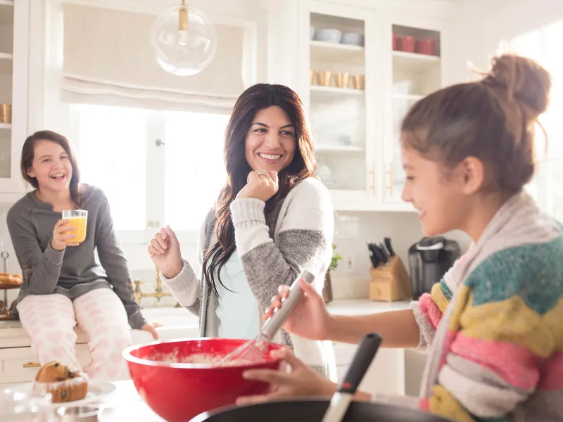 A Caucasian mom dances around the kitchen with her two daughters.