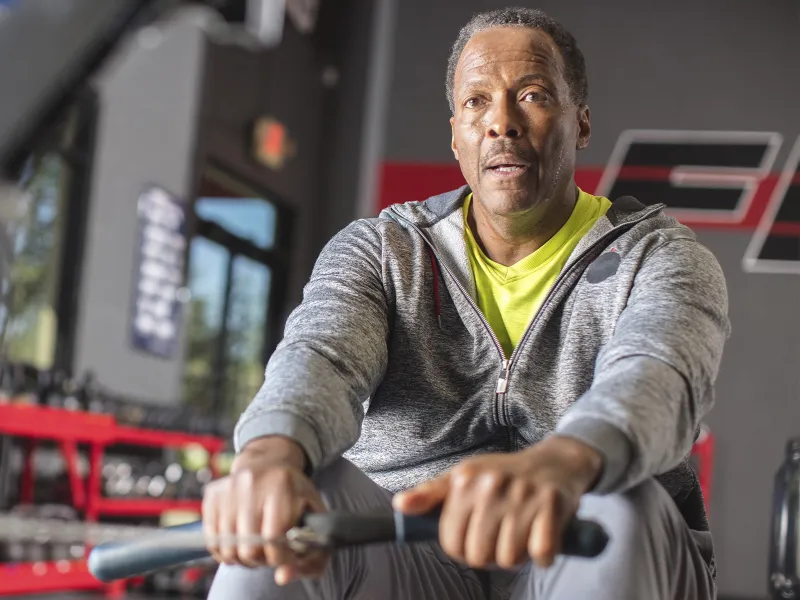 An African American man exercises on a rowing machine at the gym.