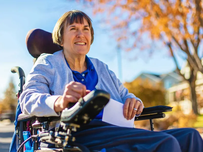 A mature woman in a wheelchair and is outside.