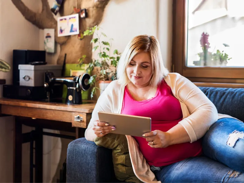 A Woman Lays on Her Couch Reading a Tablet with a Smile on Her Face.