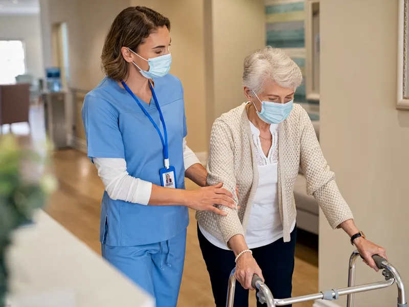 A Nurse Helps an Elderly Patient Navigate the Hallway of the Facility.	