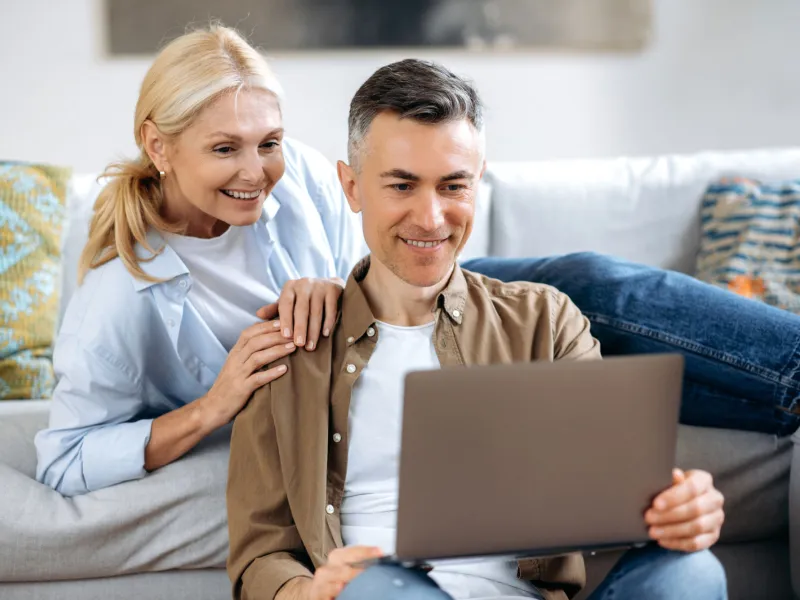 A white mature couple in their living room and on their laptop