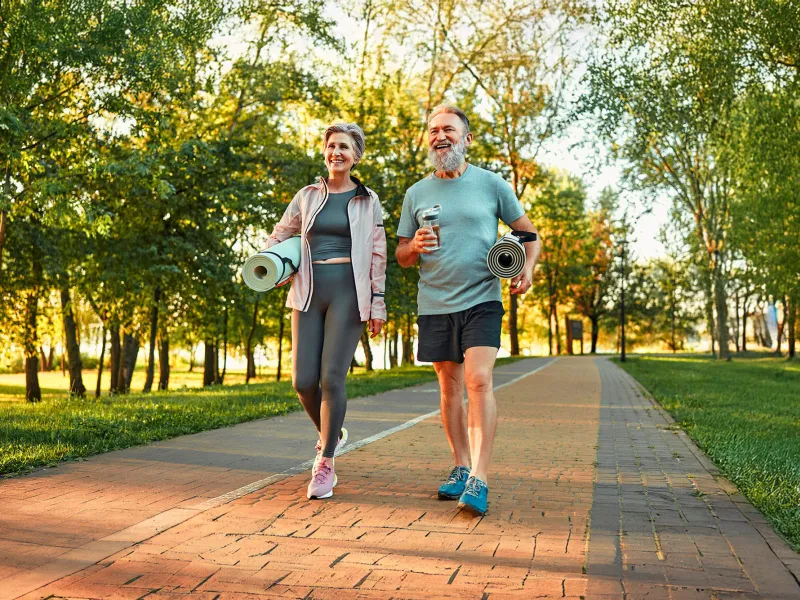 Senior Man and Woman Walking with Yoga Mats in Park