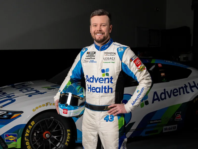 Erik Jones posing in front of his race car dressed in AdventHealth gear.