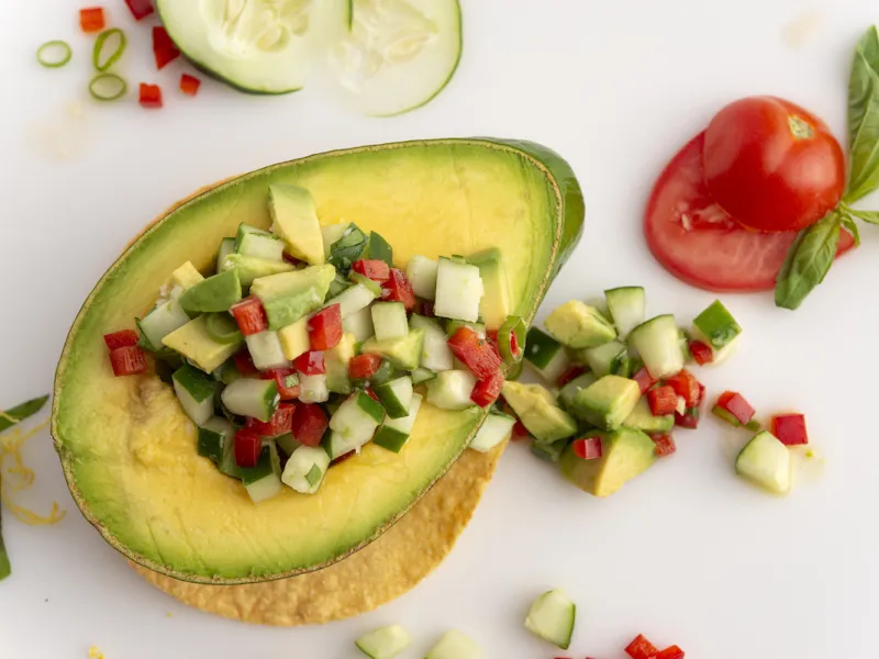 Half an avocado filled with avocado salsa on a white surface