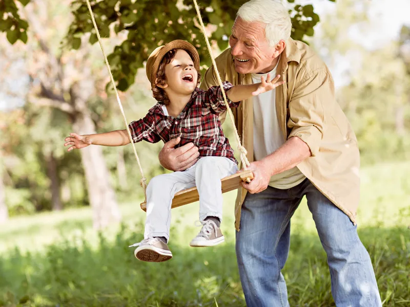 Grandfather pushing Grandchild on Swing Outdoors