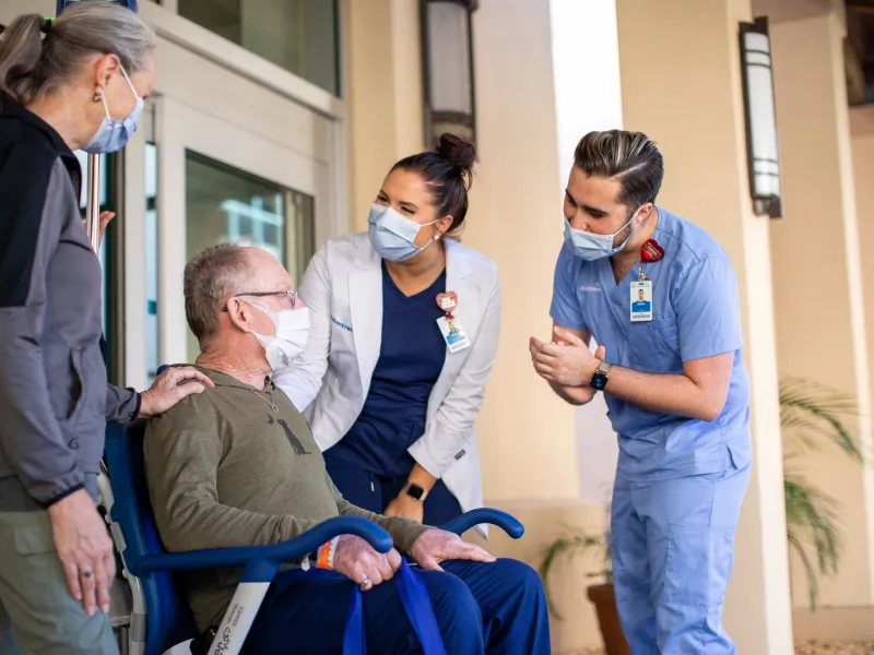 Nurses Helping Patient in Wheelchair Just Outside of the Hospital