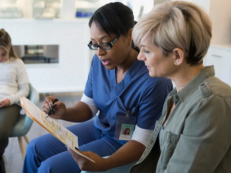 An African American nurse consults with a Caucasian female regarding her diagnosis.