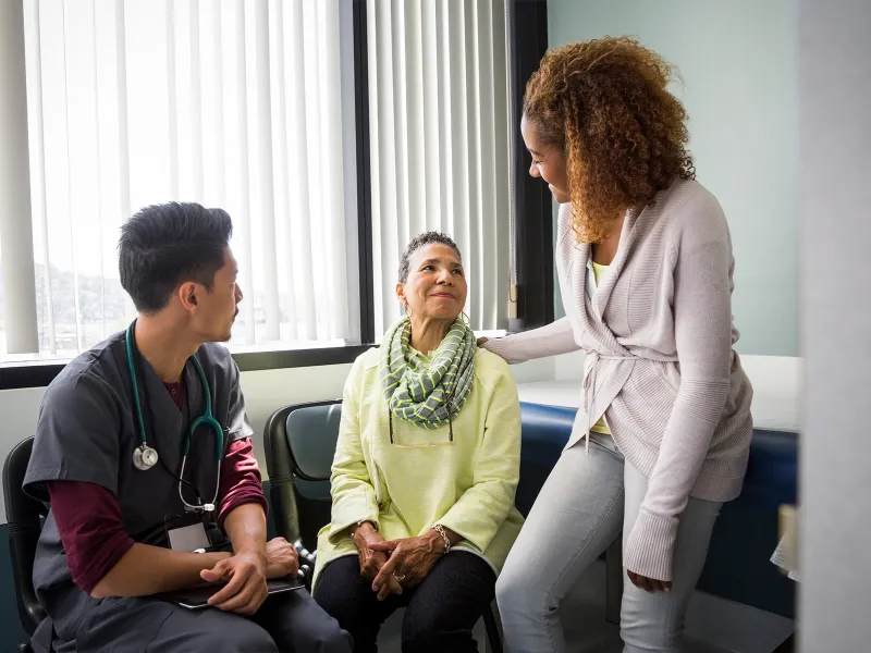 An African American daughter consoles her mother upon hearing medical news from the nurse.