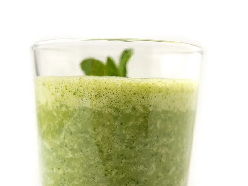 Clear glass of green smoothie with sprig on top.