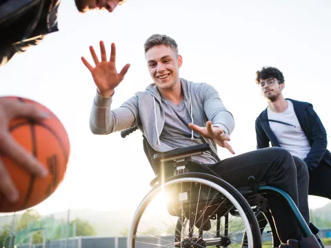 Older teens playing basketball one of which is in a wheelchair 