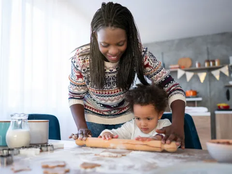 Mom and child baking cookies using rolling pin in the kitchen.
