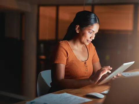 A Woman Surfs the Internet on a Table in a Dark Room of Her Home.