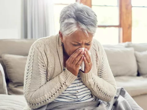 A Senior Woman Blows Her Nose from Seasonal Allergies.