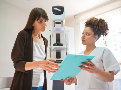 A Woman and a Provider Go Over a Chart in Front of Mammogram Machine