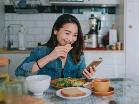 A Woman Smile at Her Mobile Device as She Eats a Balanced Breakfast
