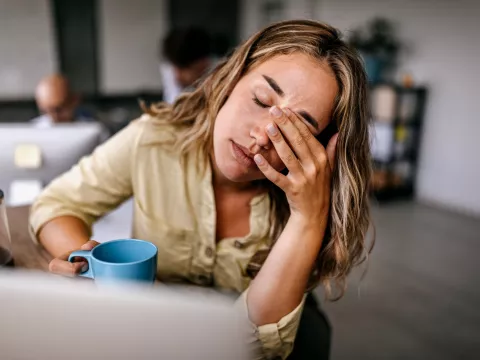 A Woman Presses Her Fingers to the Bridge of Her Nose While Drinking a Cup of Coffee at Home
