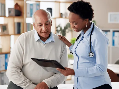 A healthcare professional shows an elderly man information on a tablet in an office setting.