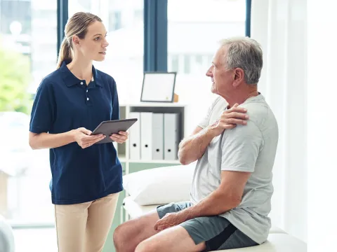 Man holding shoulder talking to woman holding tablet in office.