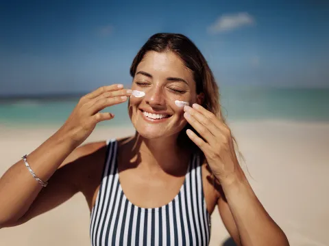 Woman applying sunscreen to her face at the beach.