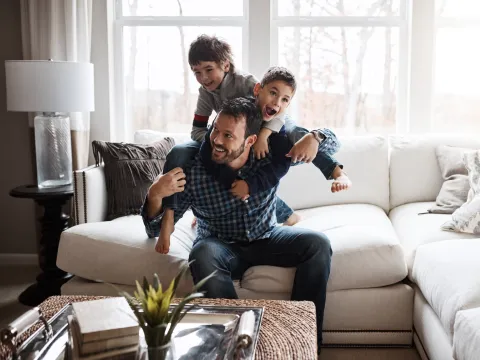 A father and his two sons playing on the sofa of their living room.