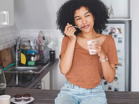 A woman sitting on her counter eating yogurt. 