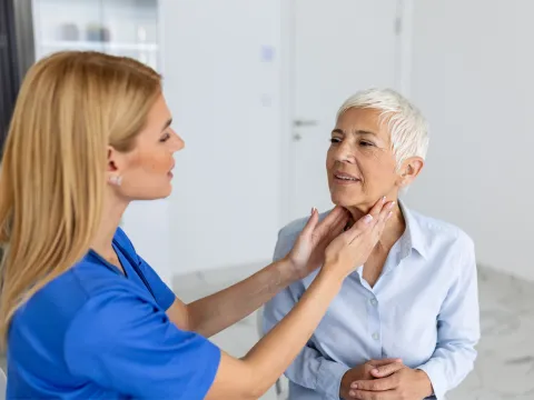 Doctor feeling the neck of a woman to check her thyroid.