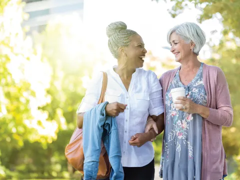 Two Women Walk Through a Park Together Drinking Coffee