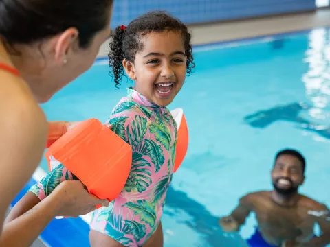 Mom helping child put on arm floats before going into pool.