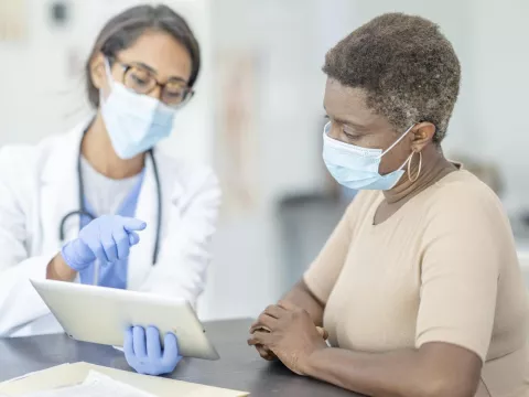 Doctor talking with patient about results on tablet, wearing masks