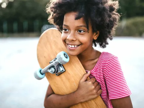 A Kid Squeezes Her Skateboard While Smiling in the Park.