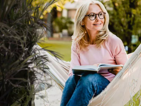 Woman sitting in hammock reading a book.