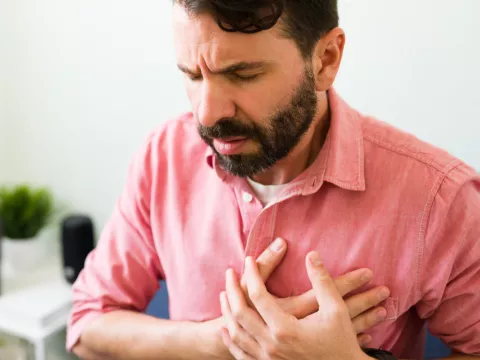 A main sitting and placing hands over chest in pain.