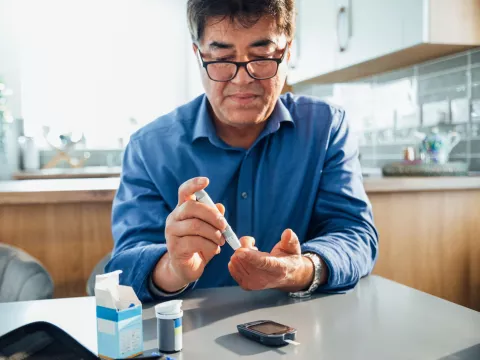 A man sitting in a kitchen using a glucose monitor.