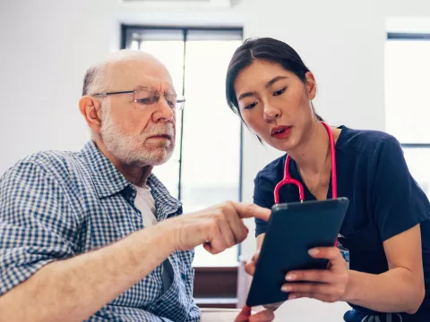An older man looks at a tablet with a nurse.