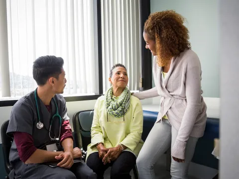 An African American daughter consoles her mother upon hearing medical news from the nurse.