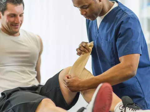Physical Therapist Bandaging Patient's Knee